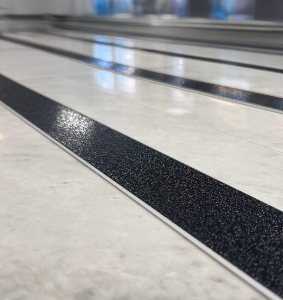 Svart aluminiumlist med halksäkert ilägg på ljust stengolv