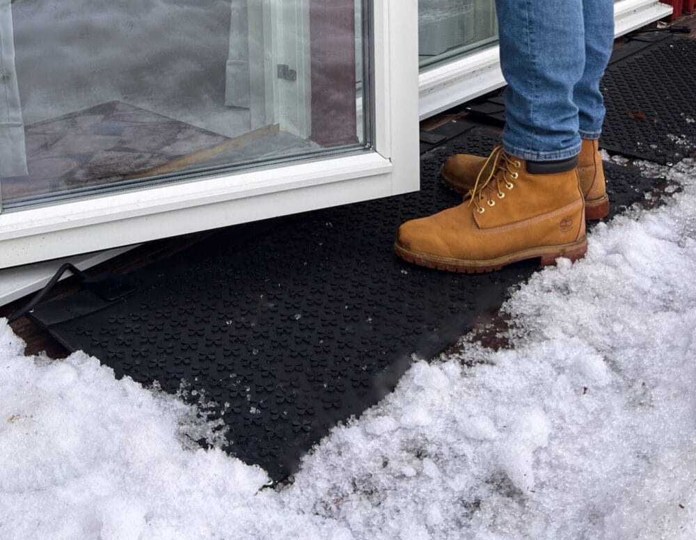 Svart snösmältningsmatta på trätrall utanför altandörr